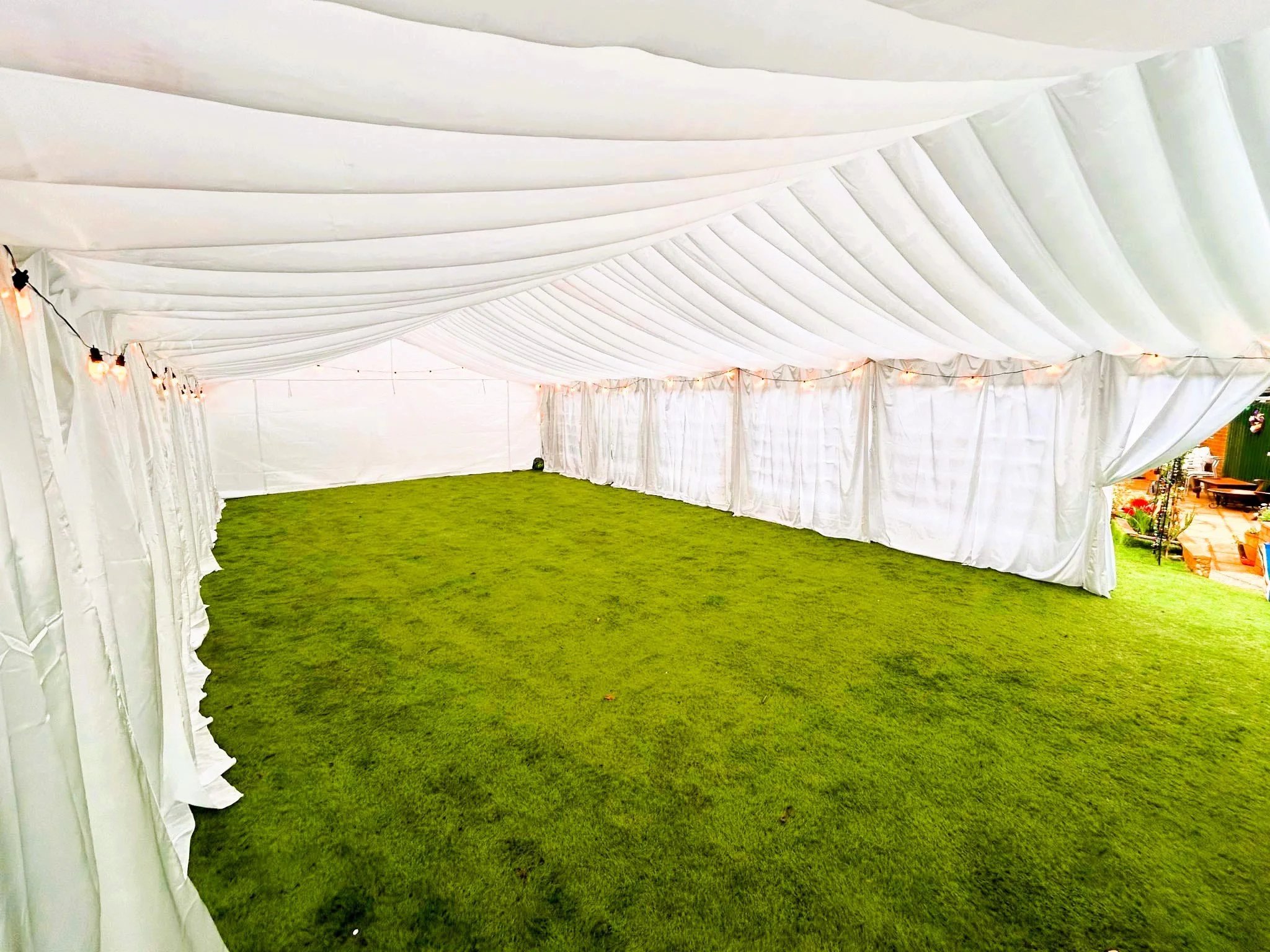 Spacious white marquee interior with draped lining and green event flooring ready for setup