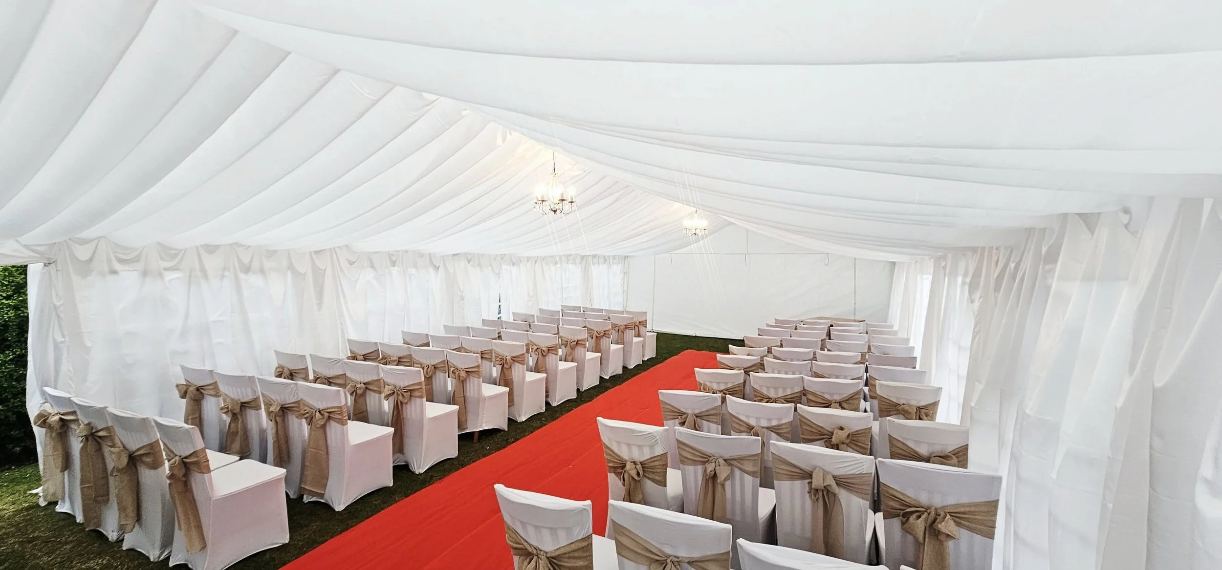 Wedding marquee ceremony setup with aisle, chairs and ivory draped interior lining