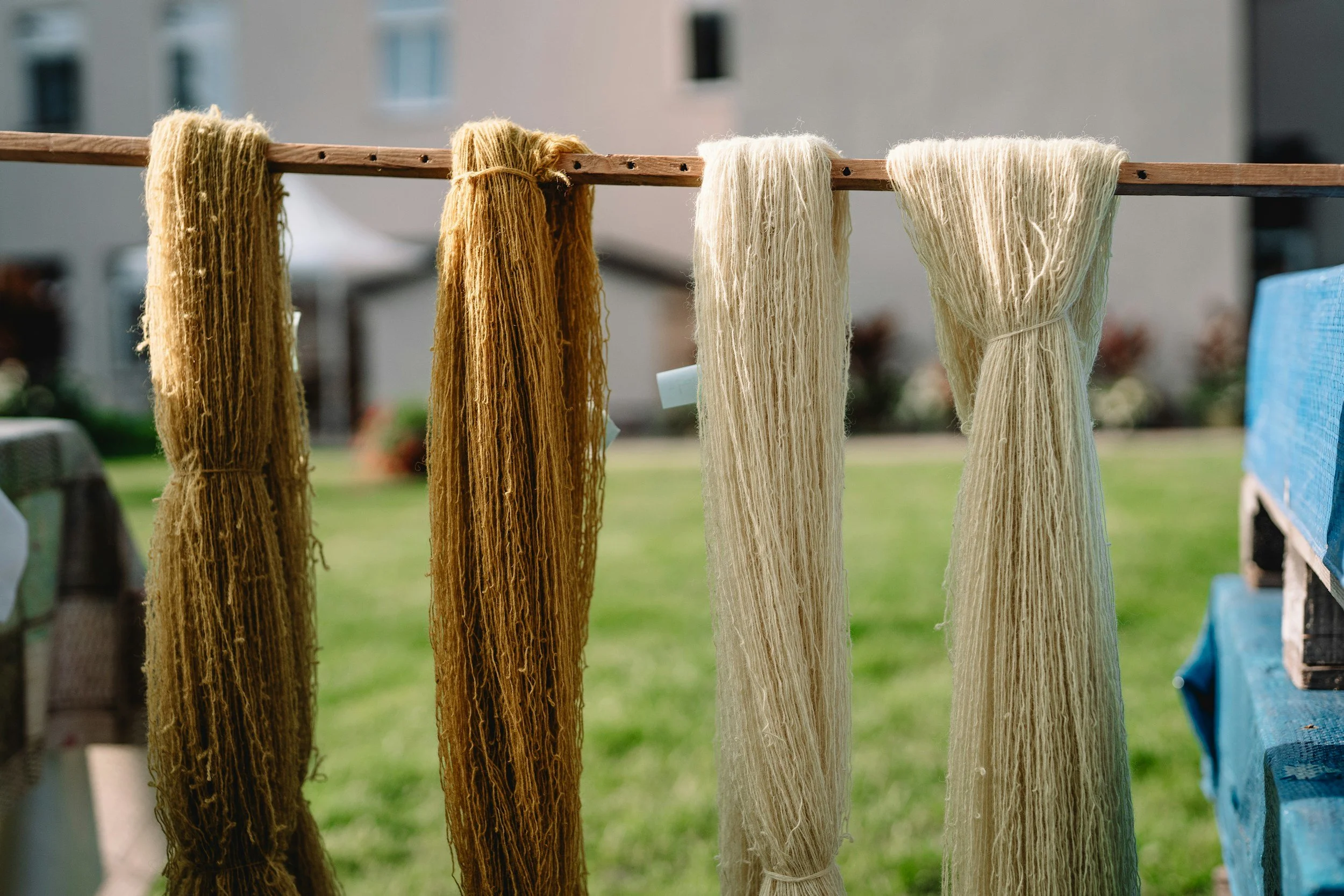 Yarn skeins hanging from a wooden rod outdoors with a blurred background.