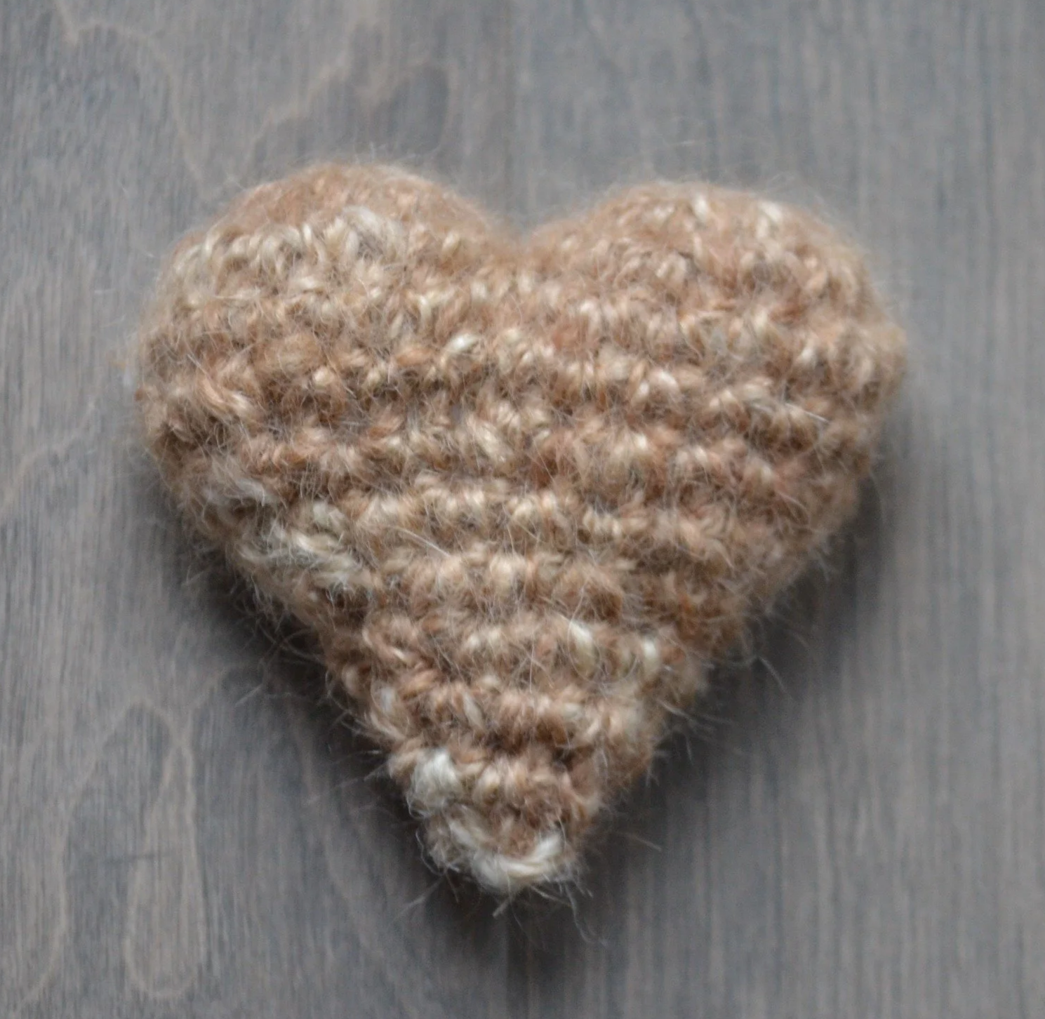 A heart-shaped, knitted, beige and cream-colored stuffed item on a gray background.