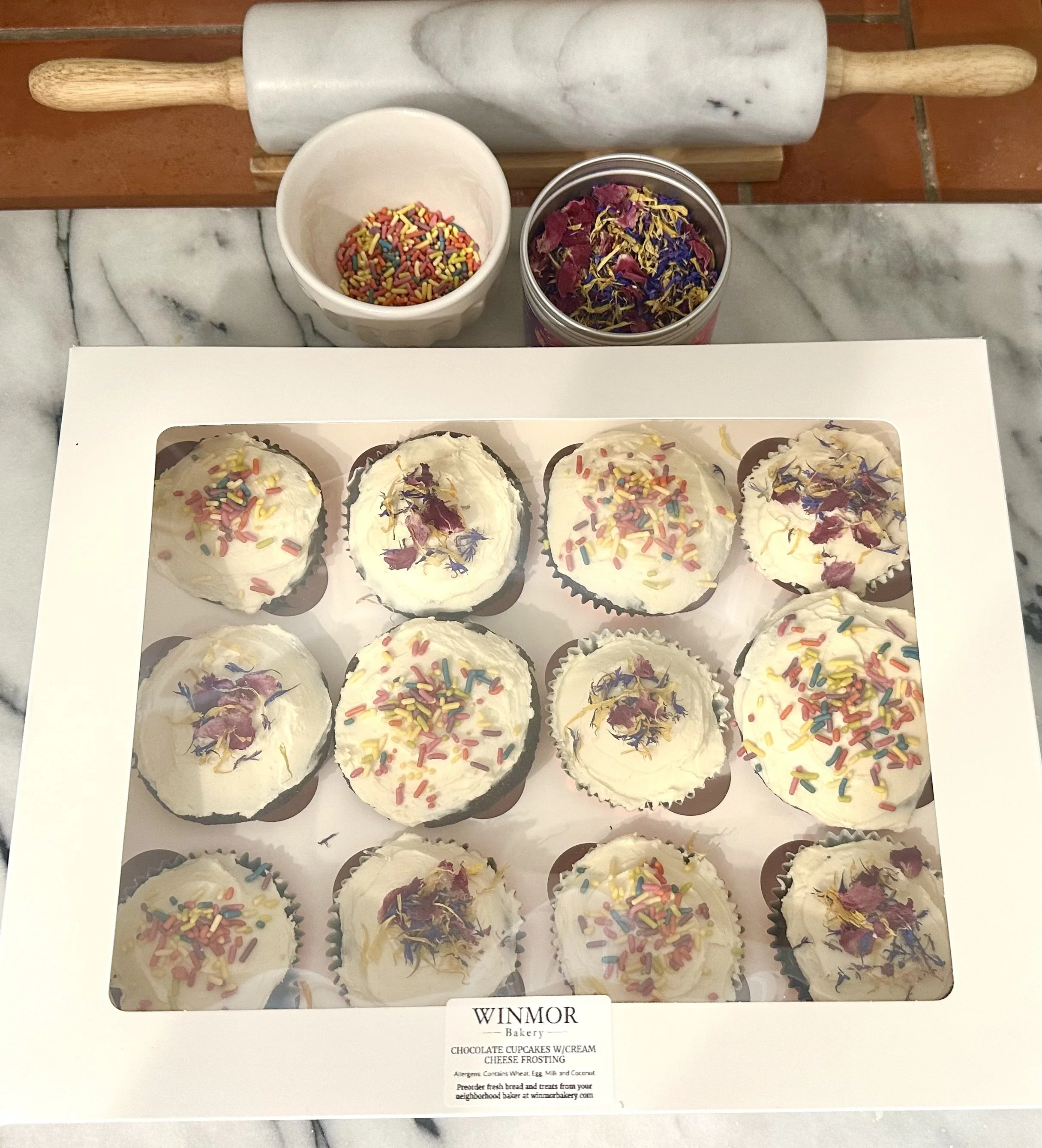 Winmor Bakery Chocolate Cupcakes in box shown with edible flowers and rainbow sprinkles. Microbakery in Tucson, AZ WinmorBakery.com