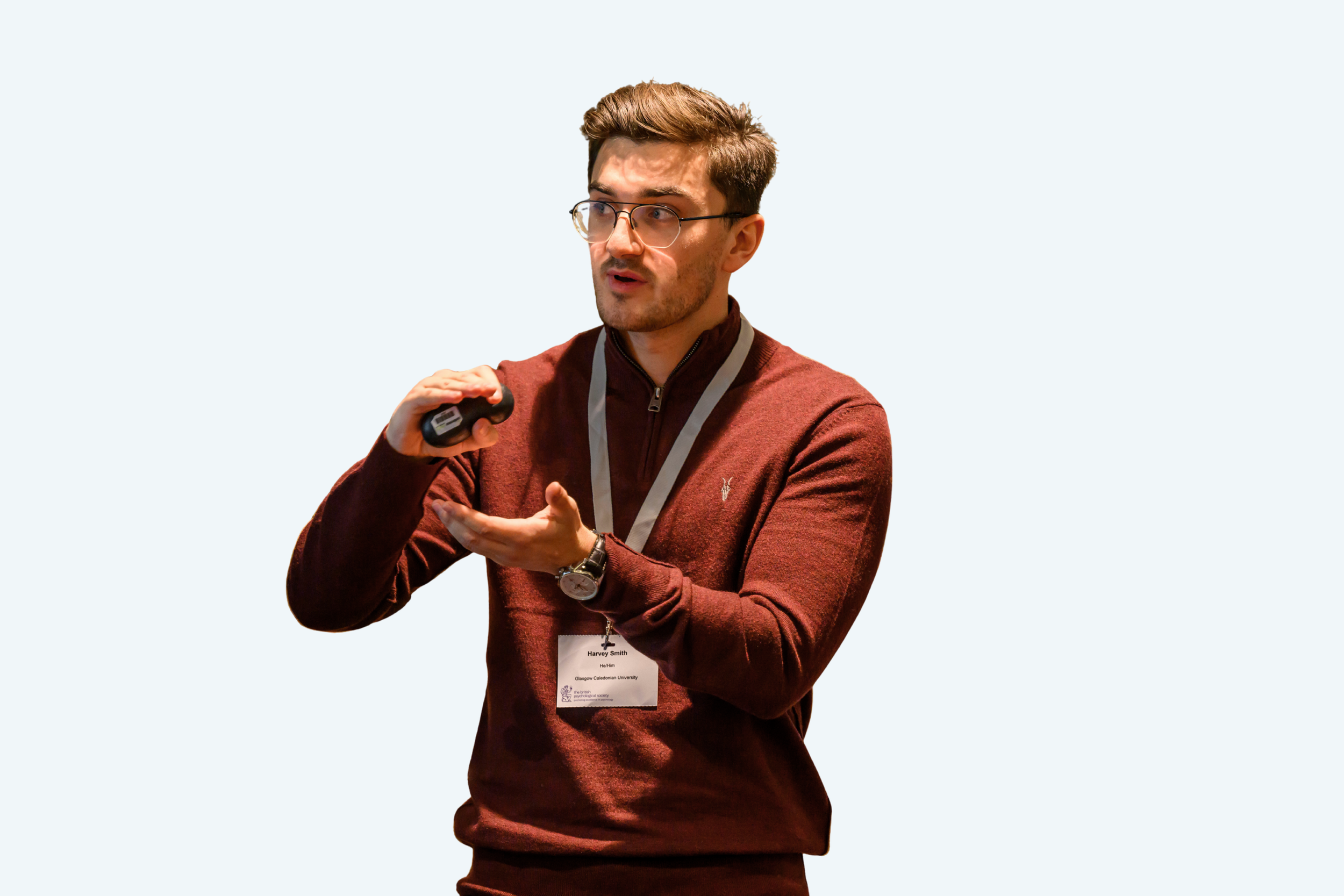 A man with glasses wearing a maroon sweater and a lanyard, pointing at his chest while speaking, against a light background.