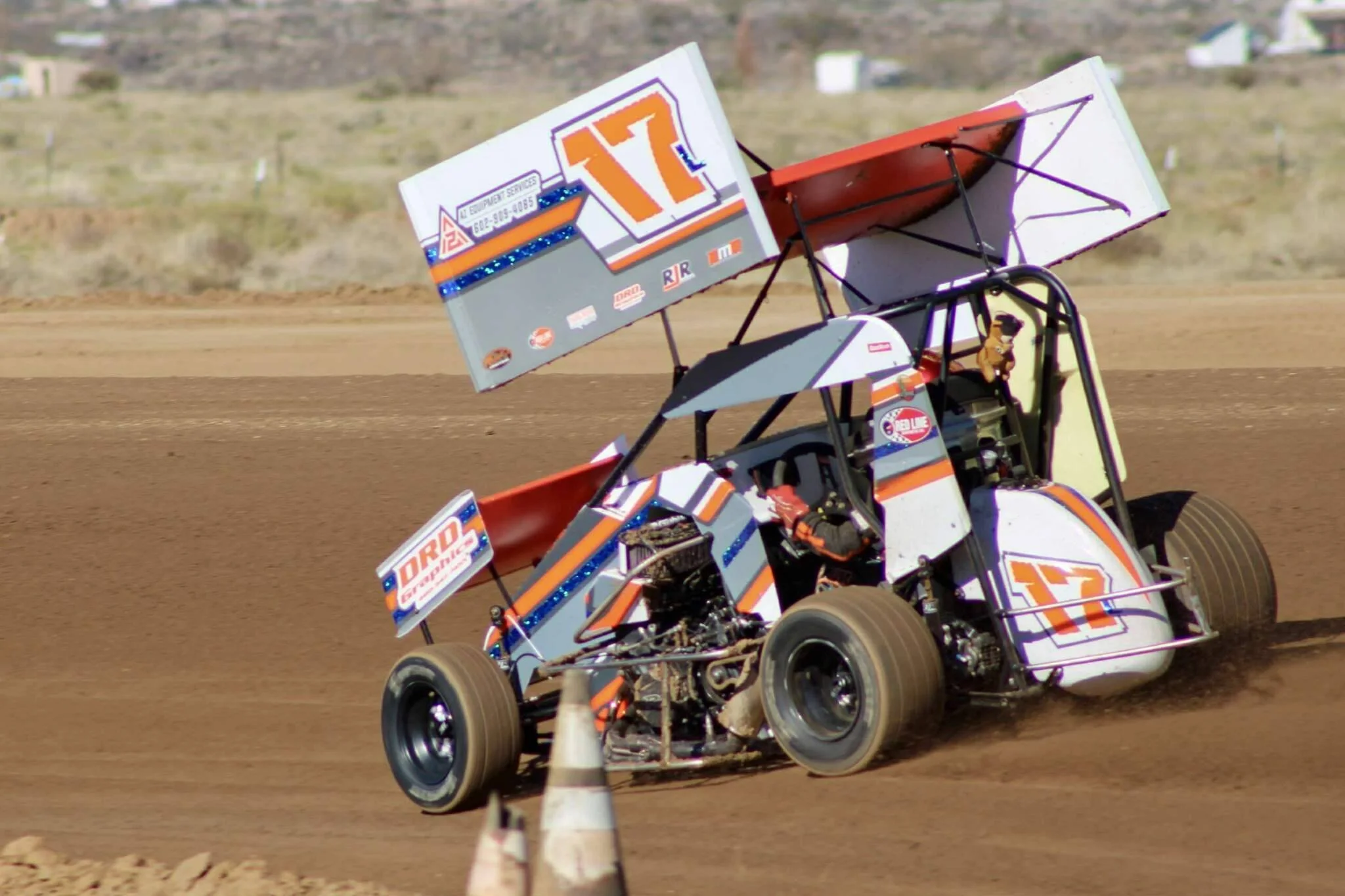 A sprint car racing on a dirt track, kicking up dust behind the vehicle.