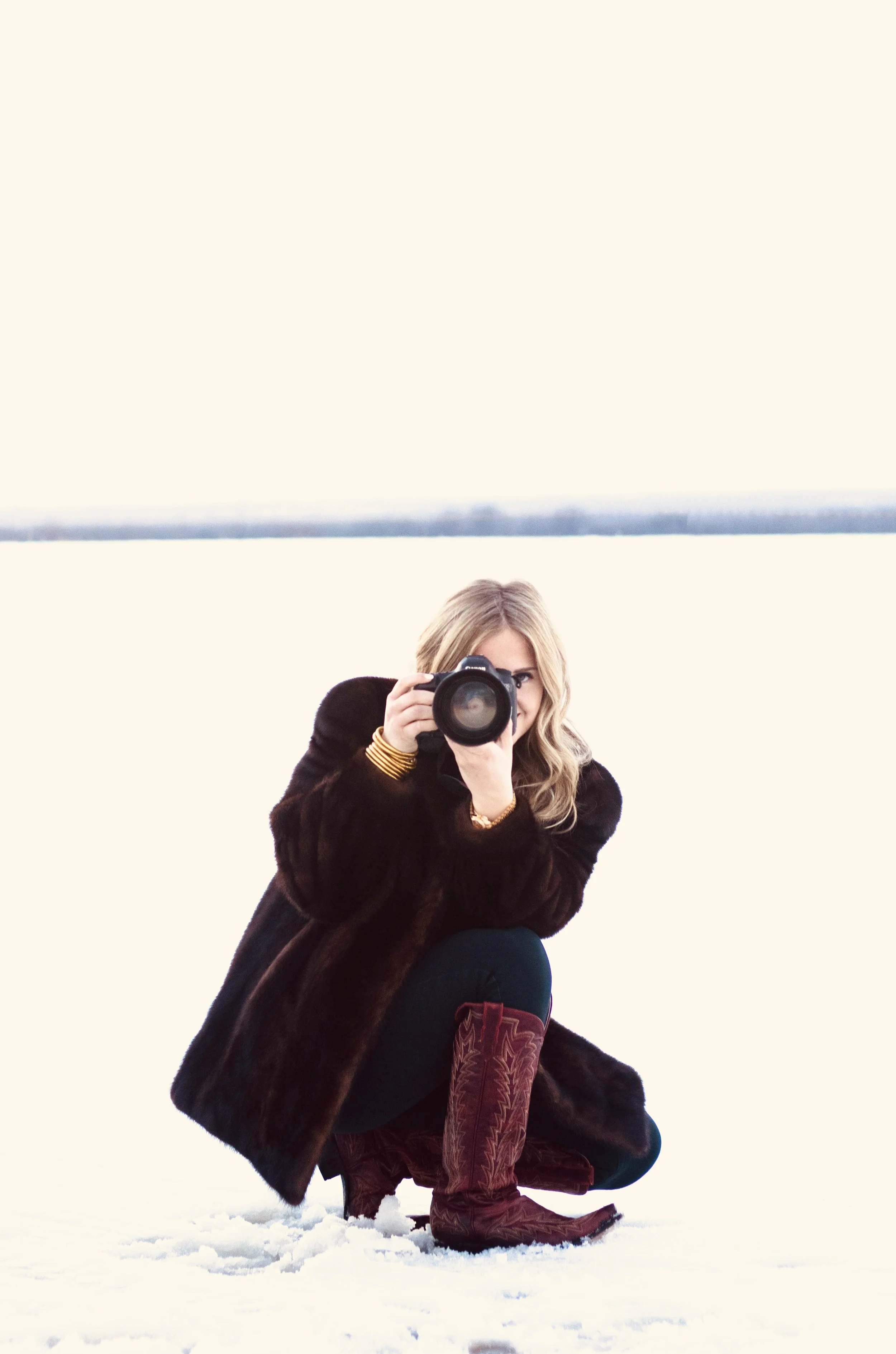 A woman crouching and taking a photo with a camera in a snowy landscape.