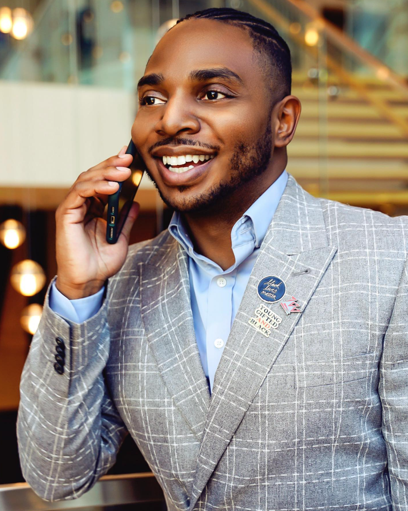 A man in a gray plaid suit talking on a cellphone, smiling, with pins on his lapel