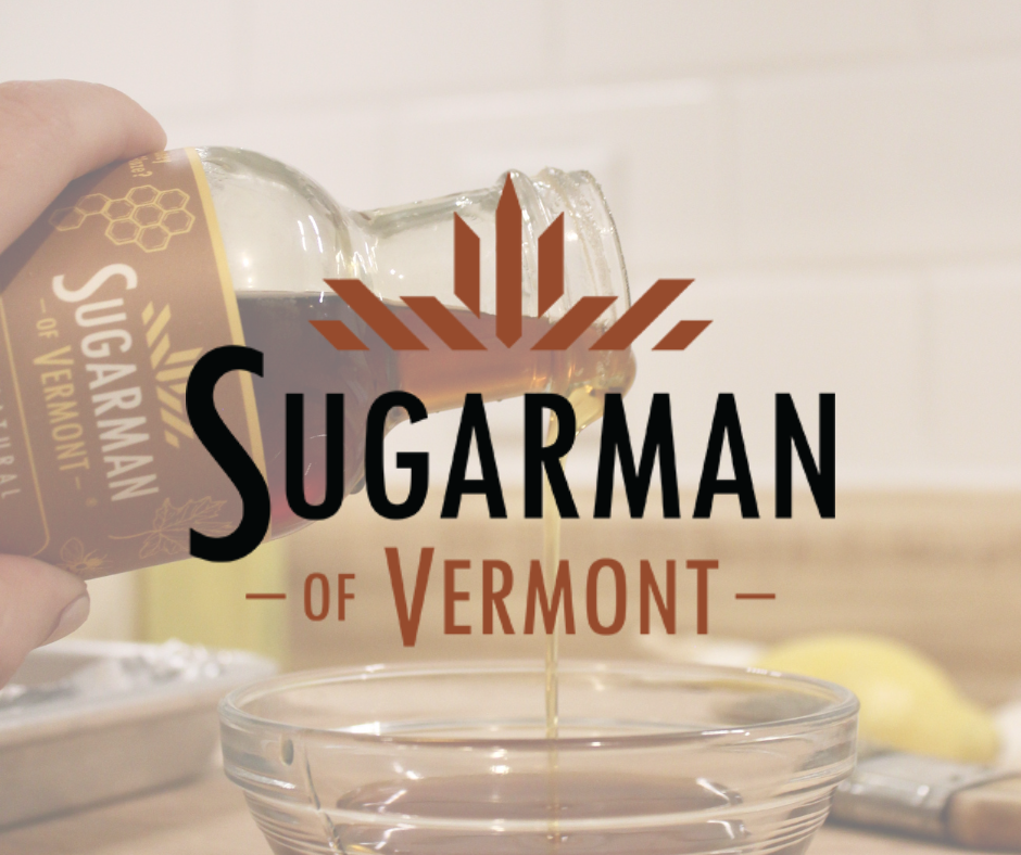 A hand pouring syrup from a glass bottle labeled 'Syrupman of Vermont' onto a glass bowl with a splash of syrup in a kitchen setting.