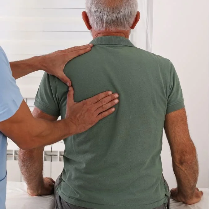 A healthcare professional examining an elderly man's shoulder in a medical setting.