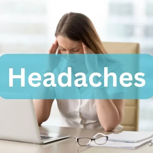 A woman sitting at a desk holding her head in pain with the word 'Headaches' overlaid on the image.