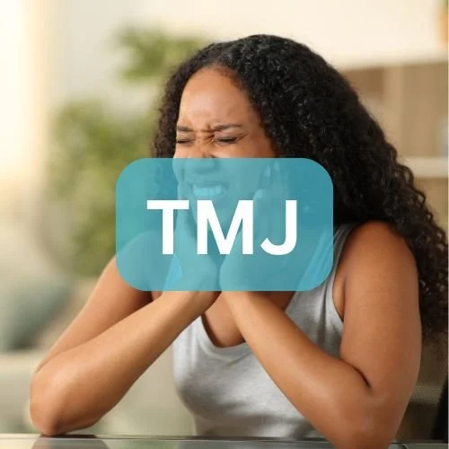 A woman with curly black hair sitting at a table, holding her throat with a distressed expression.
