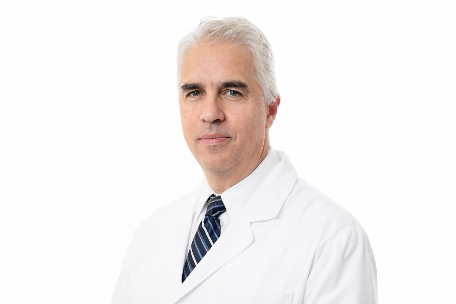 Portrait of a middle-aged male doctor with gray hair, wearing a white coat and a striped tie, standing against a white background.