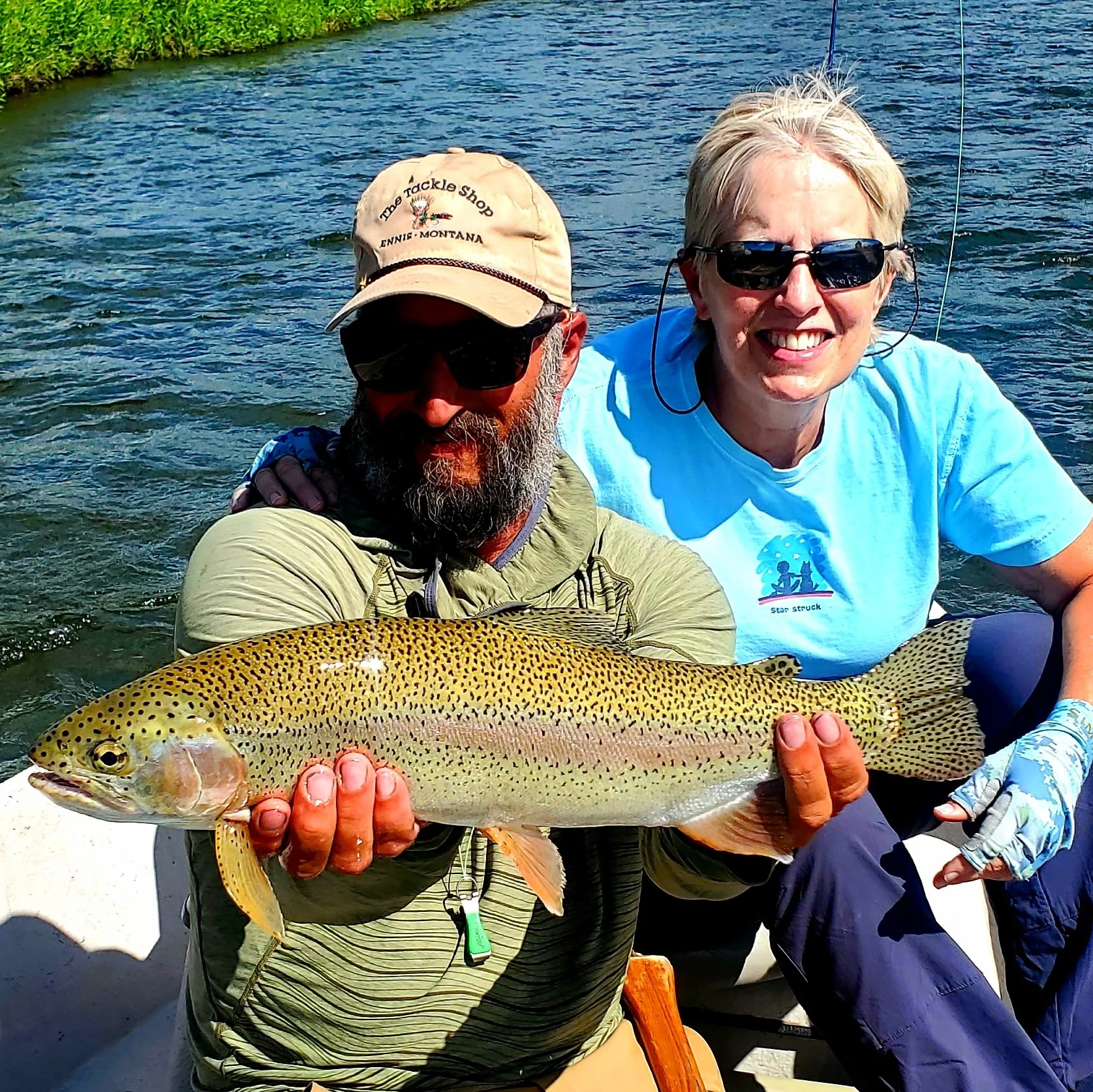 Two people in a boat holding a large fish, with water in the background.