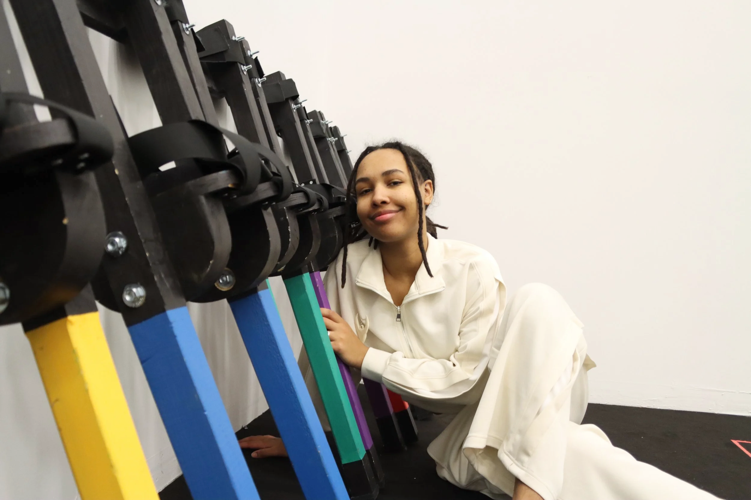 Pixel Heller sitting next to colorful stilts in a white room.