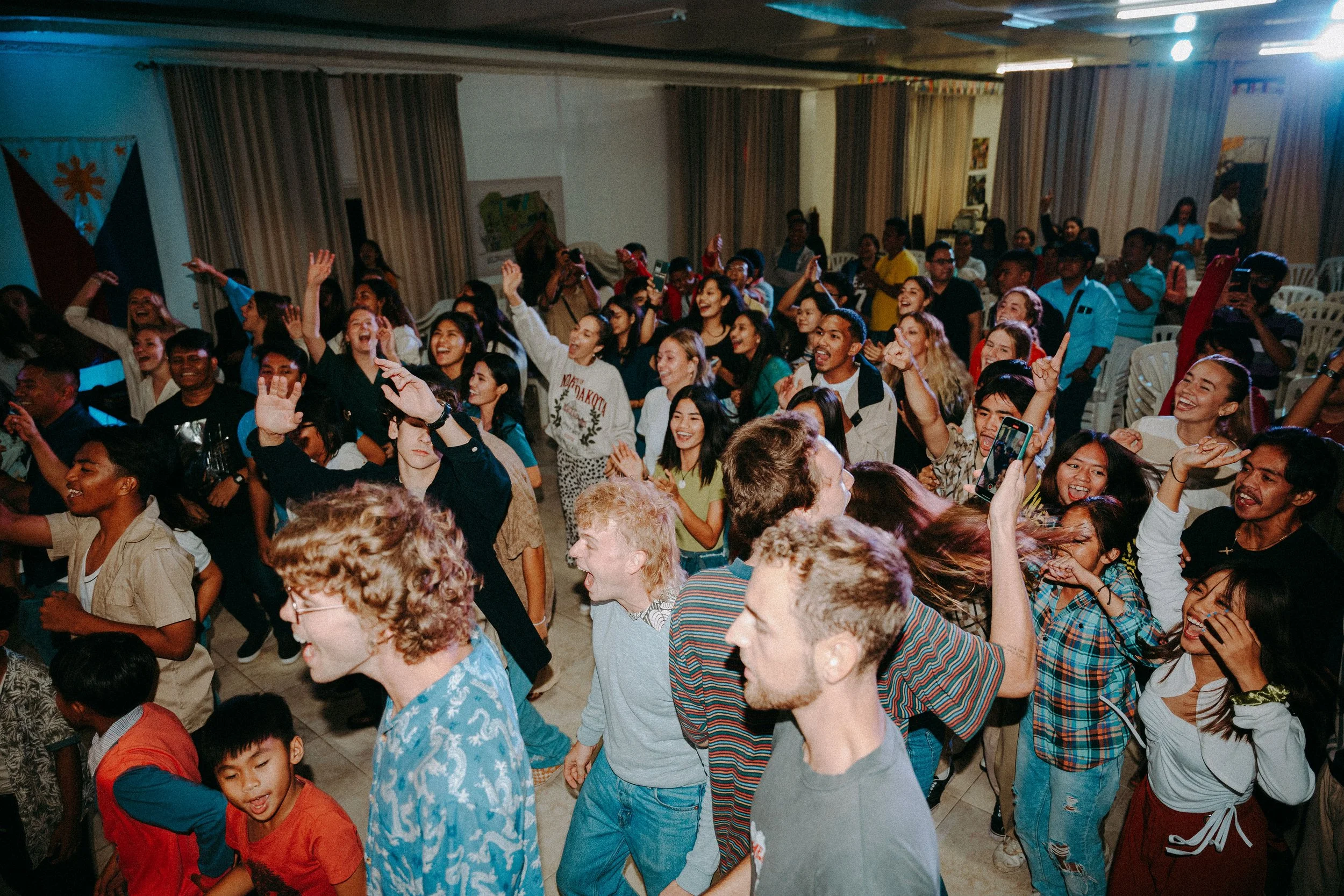 A lively indoor gathering with diverse people dancing, smiling, and enjoying themselves.