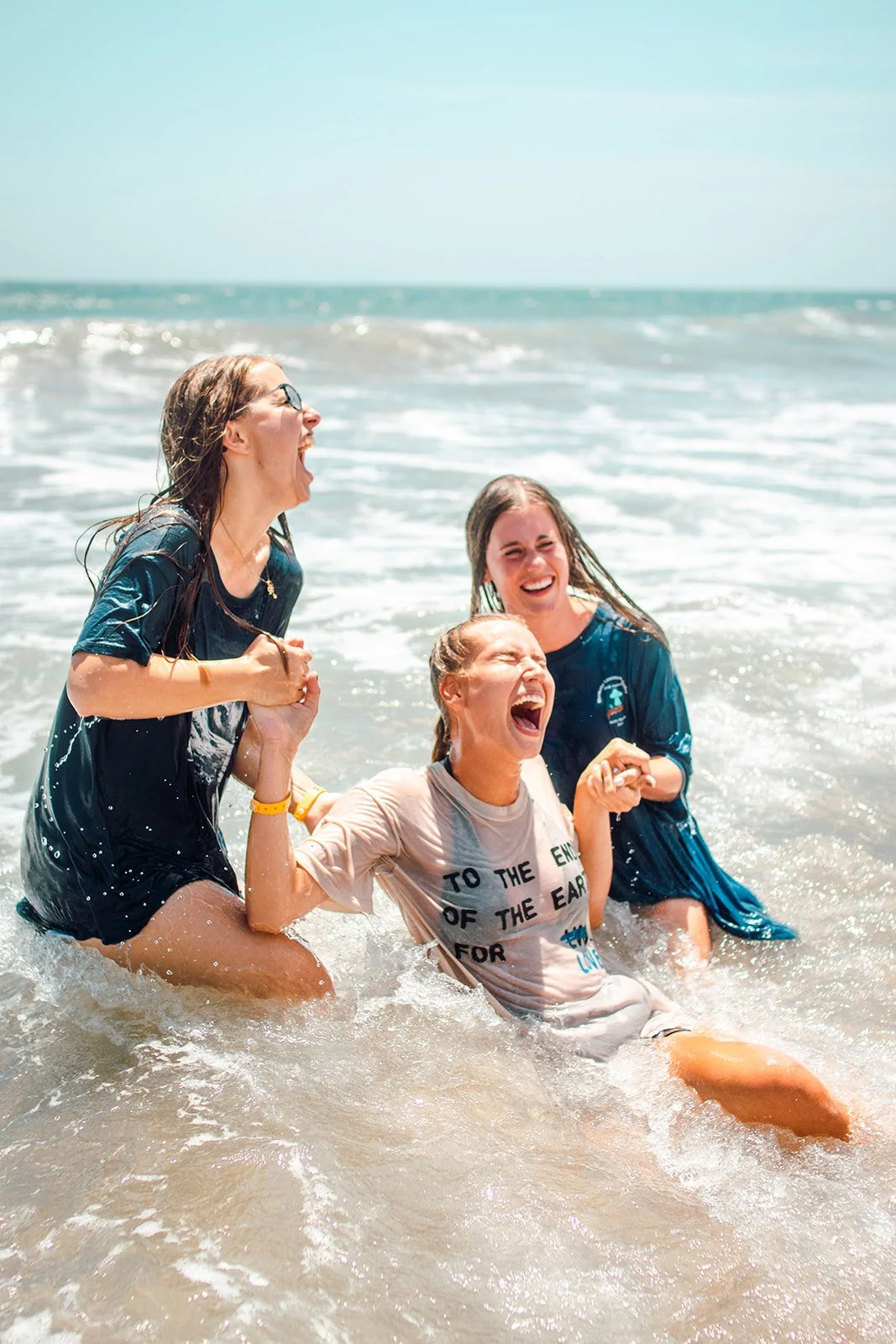 Four women laughing and enjoying a swim in the ocean on a sunny day.