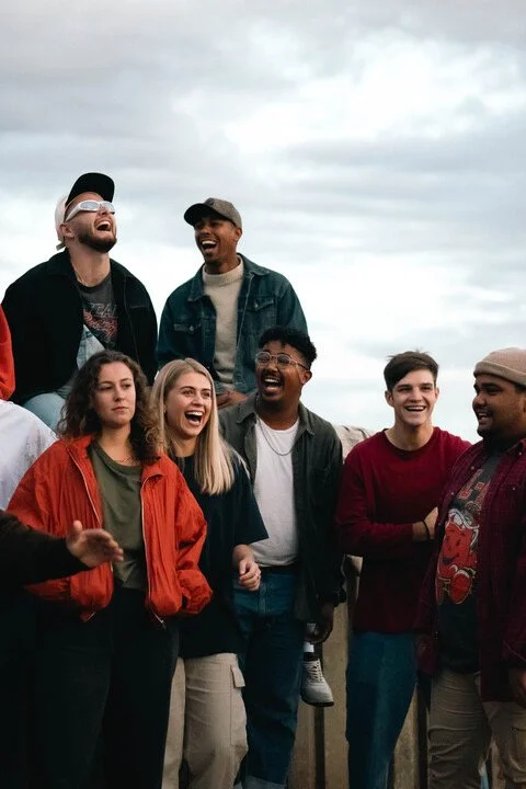Four children stand and sit along a dirt road next to a field of corn with hills in the background.