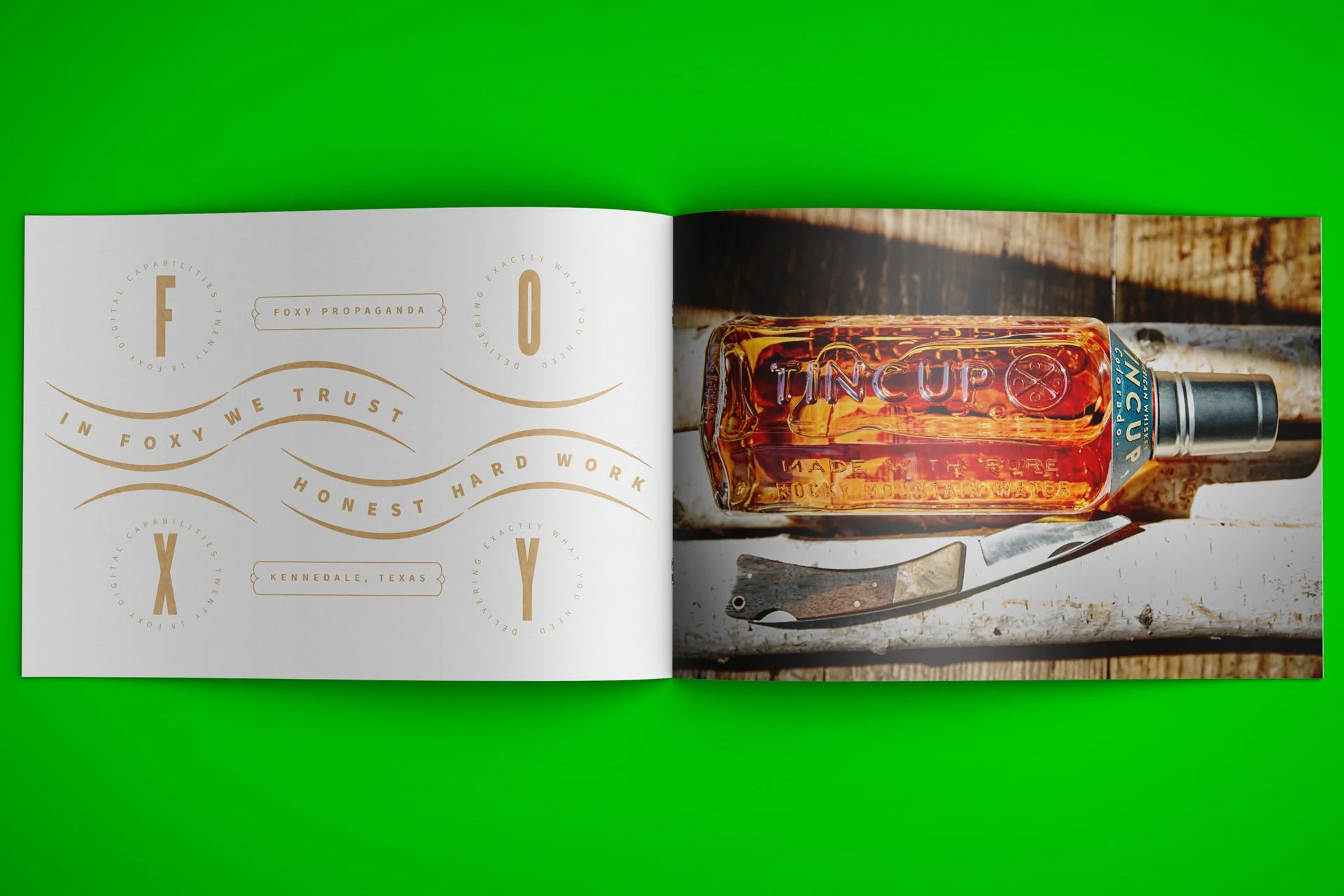 Open magazine with a left page featuring gold text and symbols related to faith and hard work, and a right page displaying a bottle of Tincup whiskey, a corkscrew, and a rustic wooden background, set on a bright green surface.