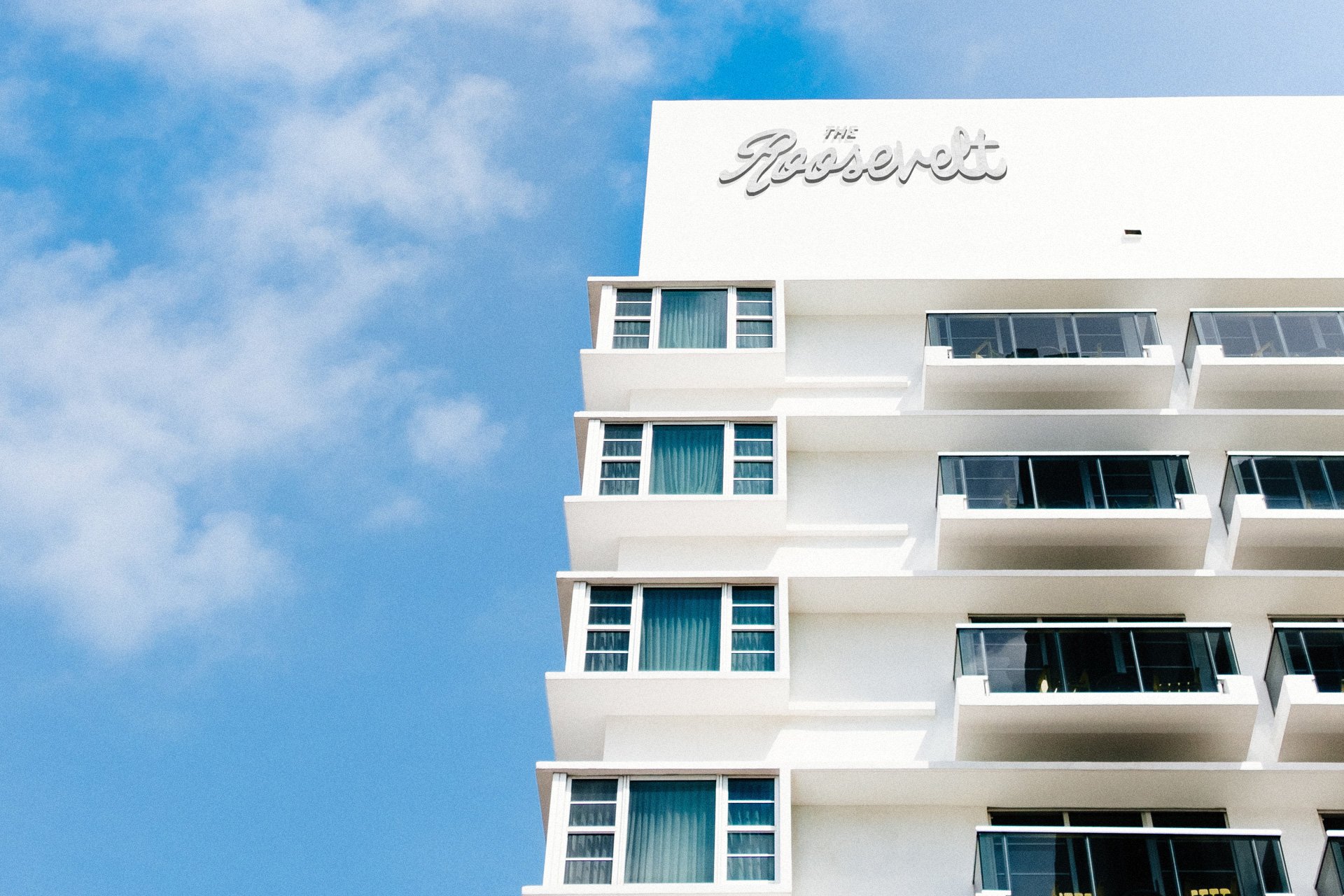 The facade of a white hotel building named 'The Grosvenor' with balconies and large windows, set against a blue sky with some clouds.