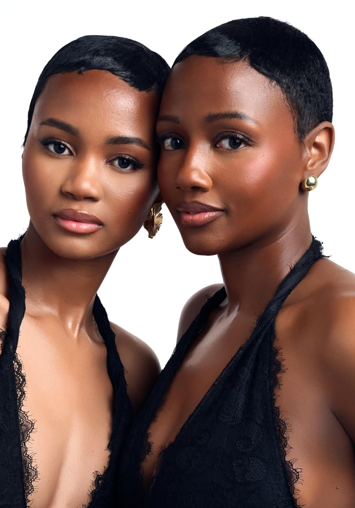 Two women with short, sleek black hair, wearing black lace tops and gold earrings, posing close together against a white background.