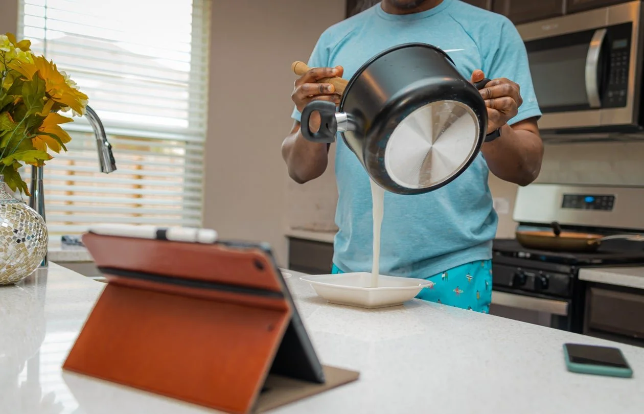 A woman and two children making crafts at a table with paper, scissors, and decorative items in a colorful classroom.