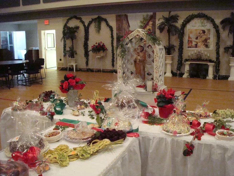 Decorated table with gifts, flowers, and a nativity scene in a hall with wall art and plants.