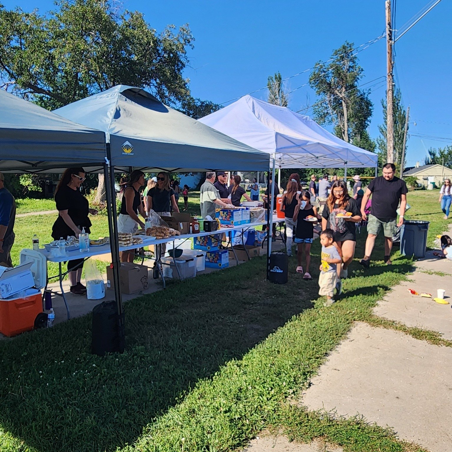 People gathered at outdoor tents selling food and snacks, with children and adults walking and socializing on a sunny day.