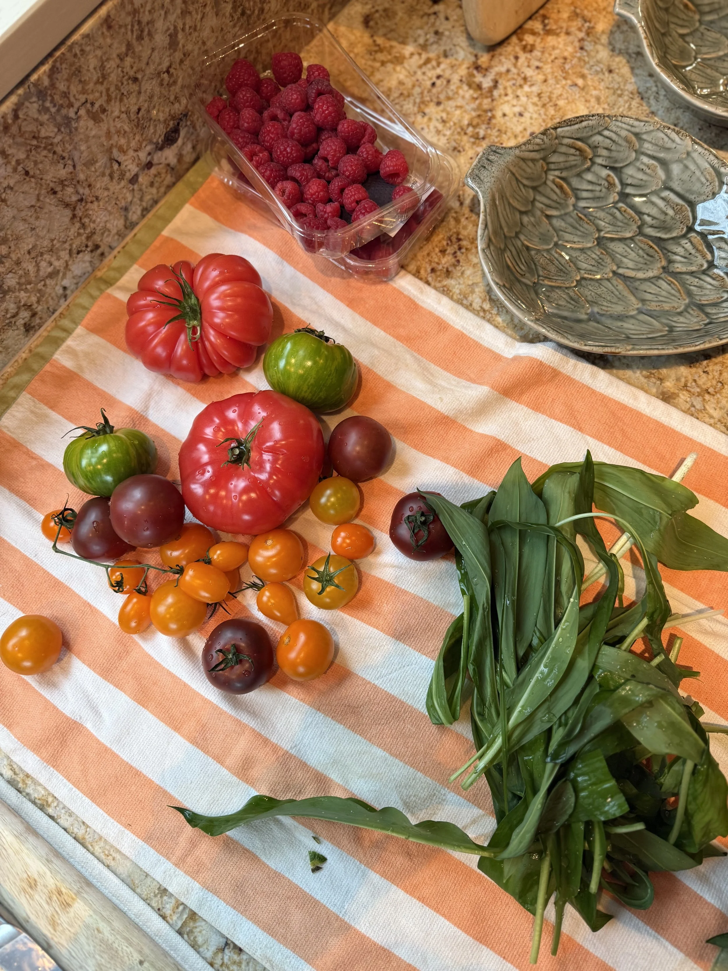 Fresh tomatoes, basil, raspberries, and blueberries on a kitchen counter with bowls.