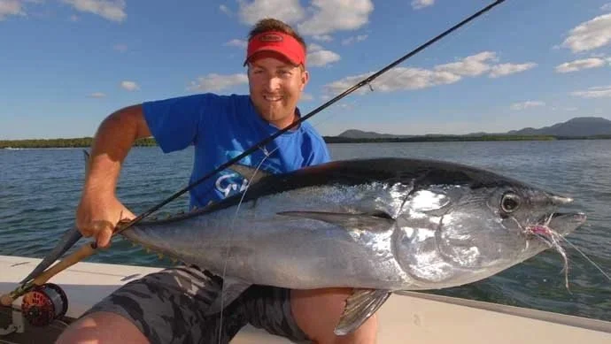 Man in blue shirt and red cap on boat holding a large fish he caught while fishing on a lake or river.
