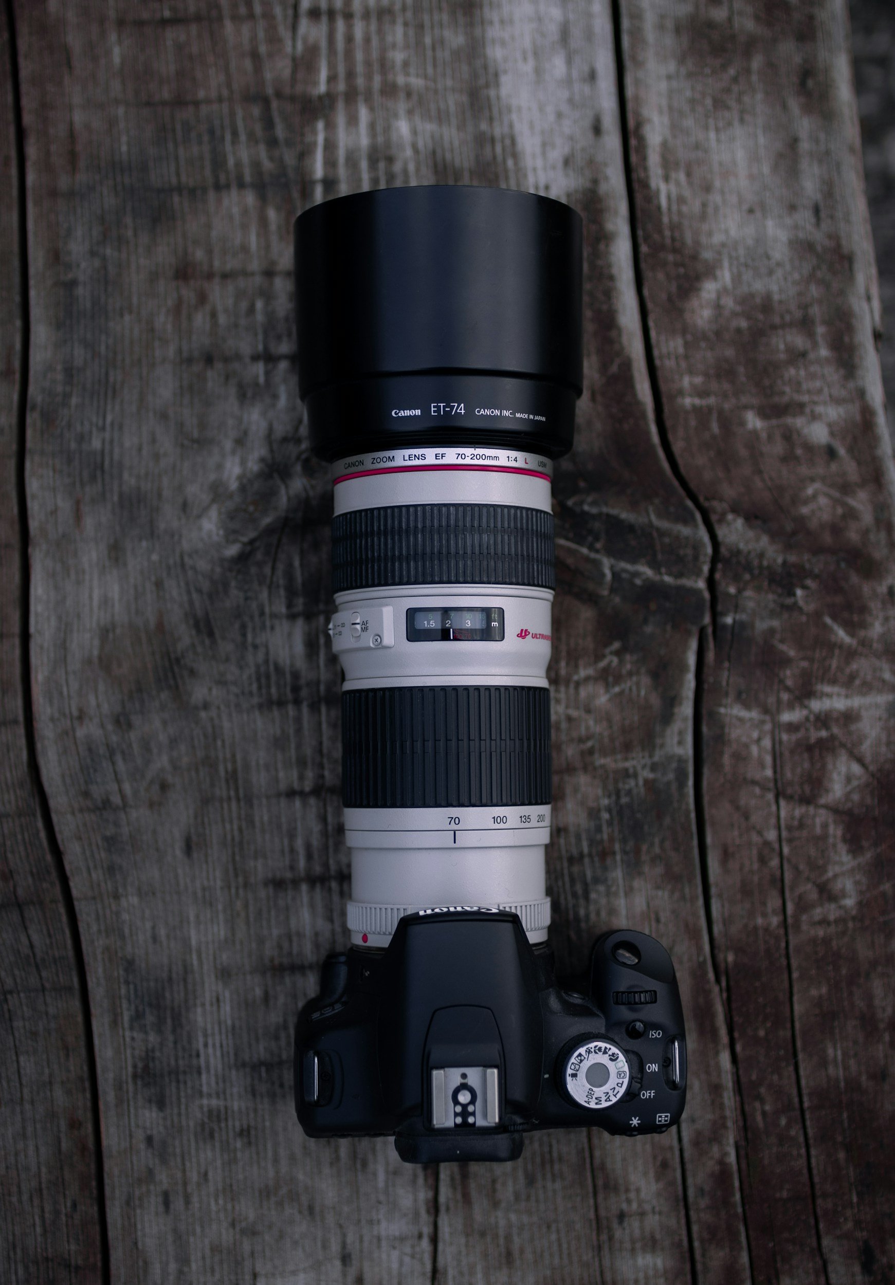 A professional camera with a large telephoto lens attached, placed on a weathered wooden surface.