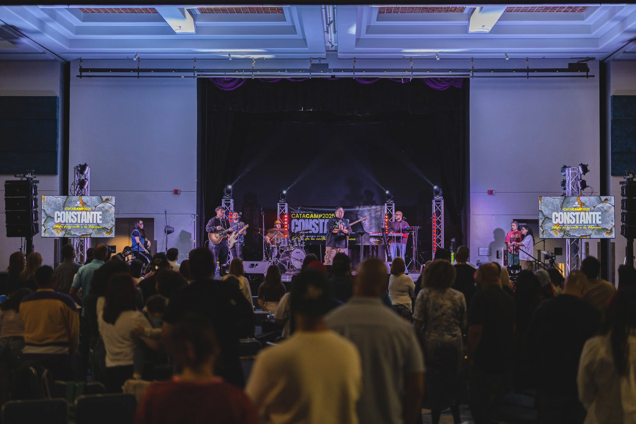 Musicians performing on stage at the Catacamp 2025 event, with a crowd of attendees watching in a large indoor venue.