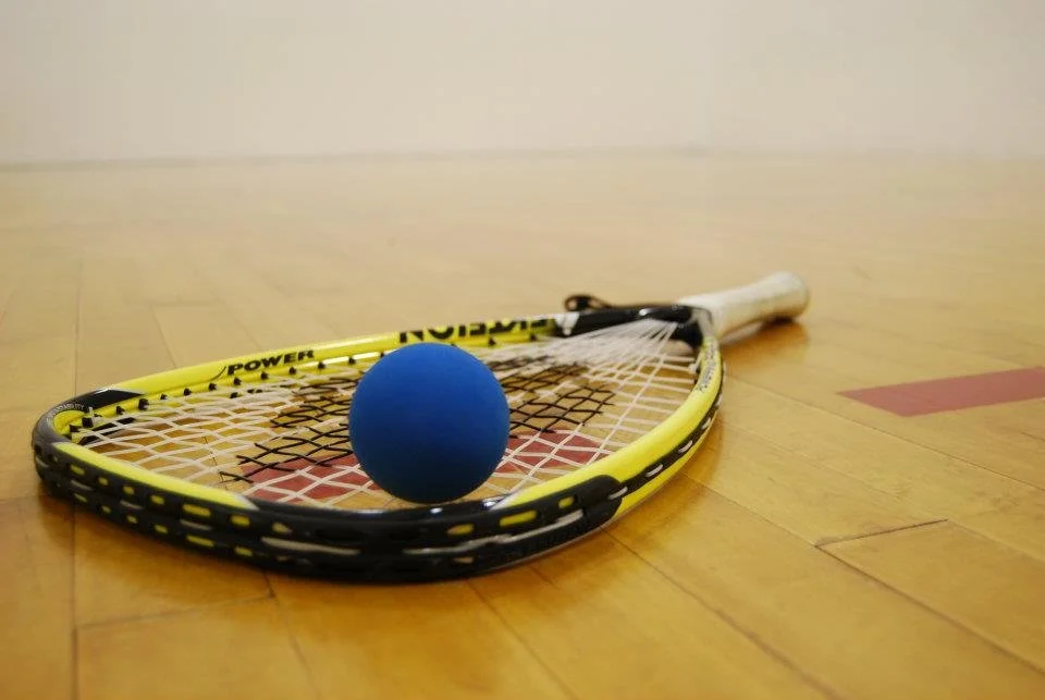 A floor tennis racket with a blue ball on a hardwood court.