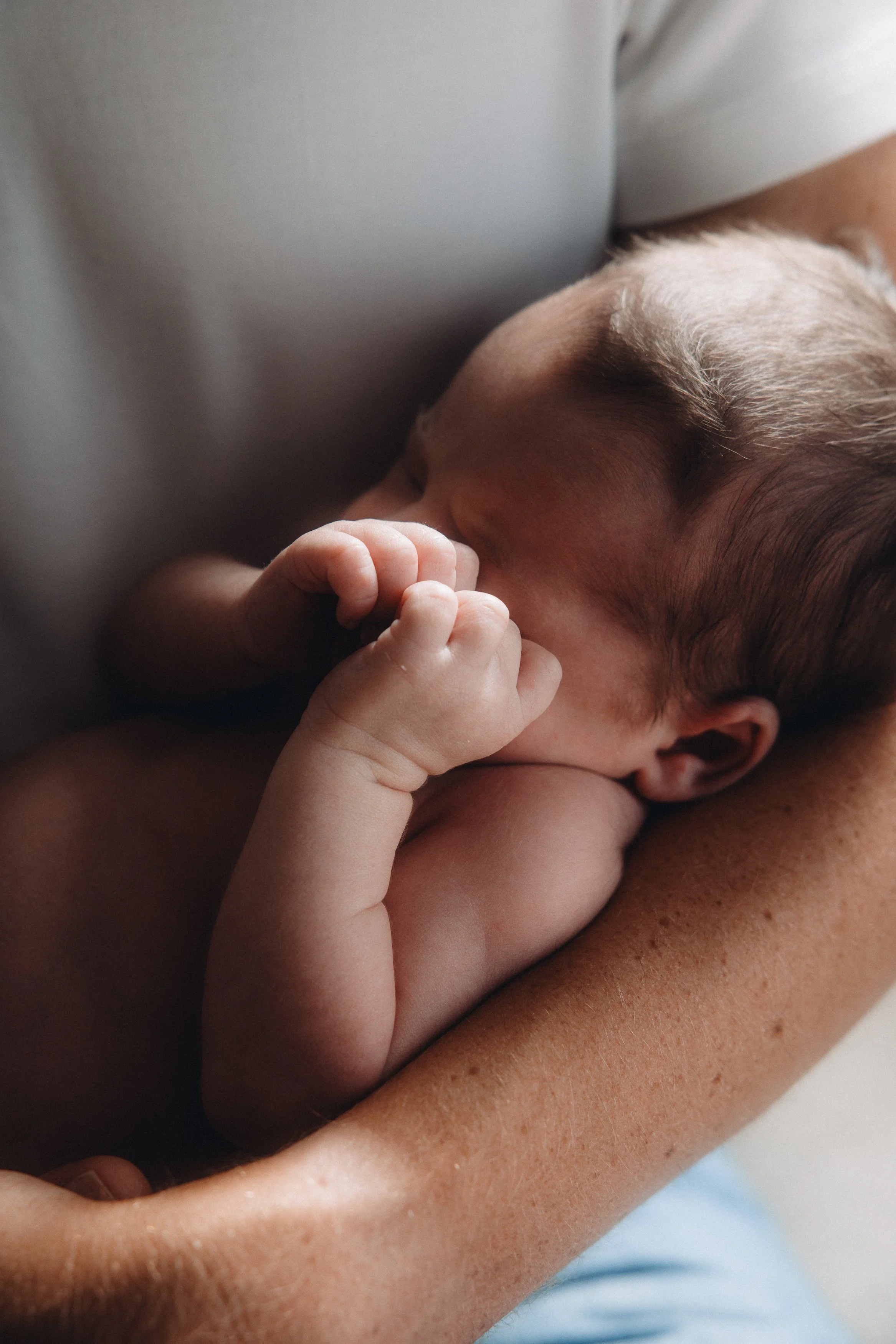 Nærbilde av en baby som sover, holdende sin finger nær ansiktet.