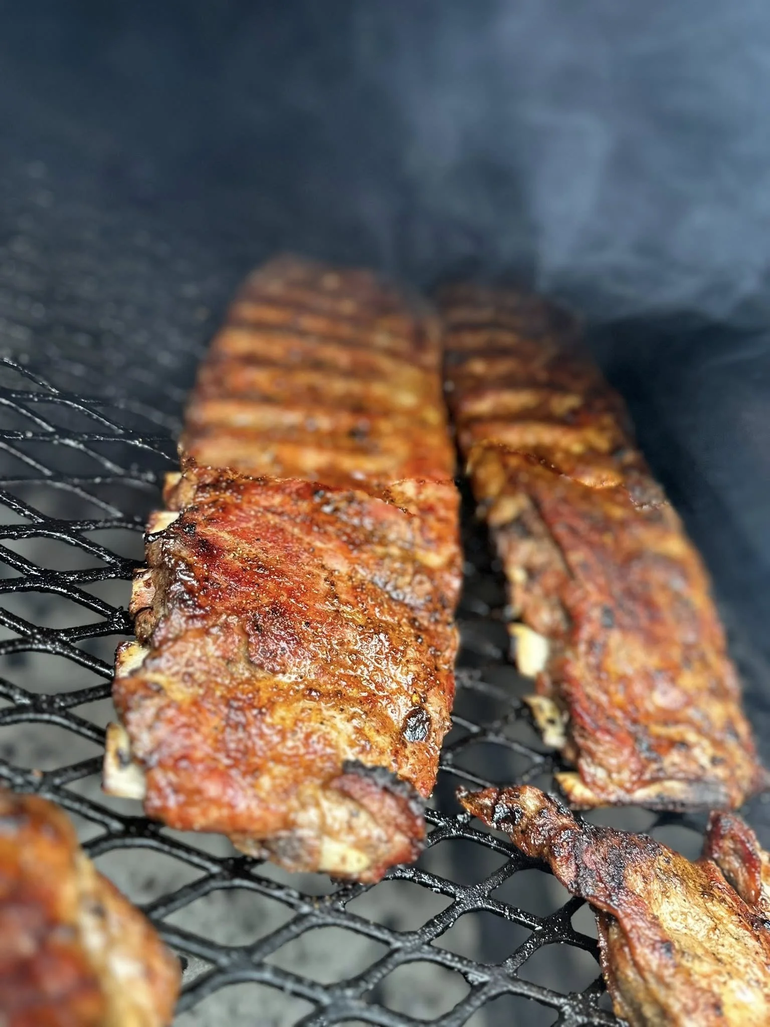 Close-up of ribs cooking on a grill, with a smoky background.
