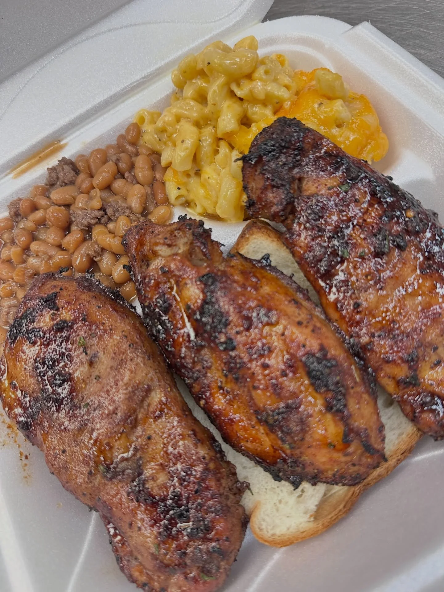 Barbecue chicken thighs on bread with baked beans, macaroni and cheese, and sliced baked potato.