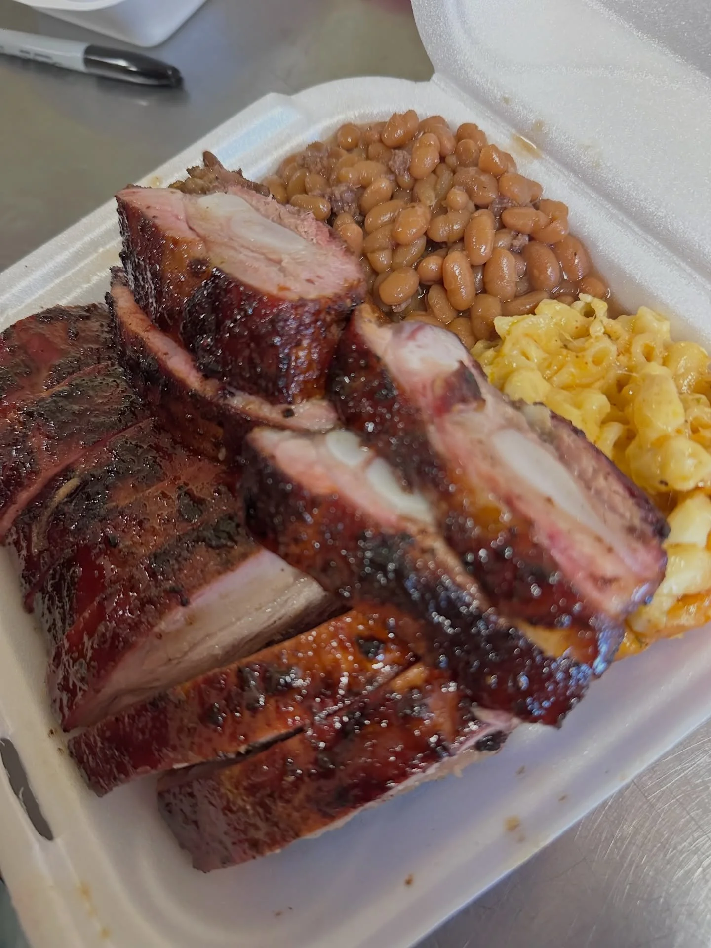 Barbecue pork ribs with baked beans and macaroni and cheese in a takeout container.