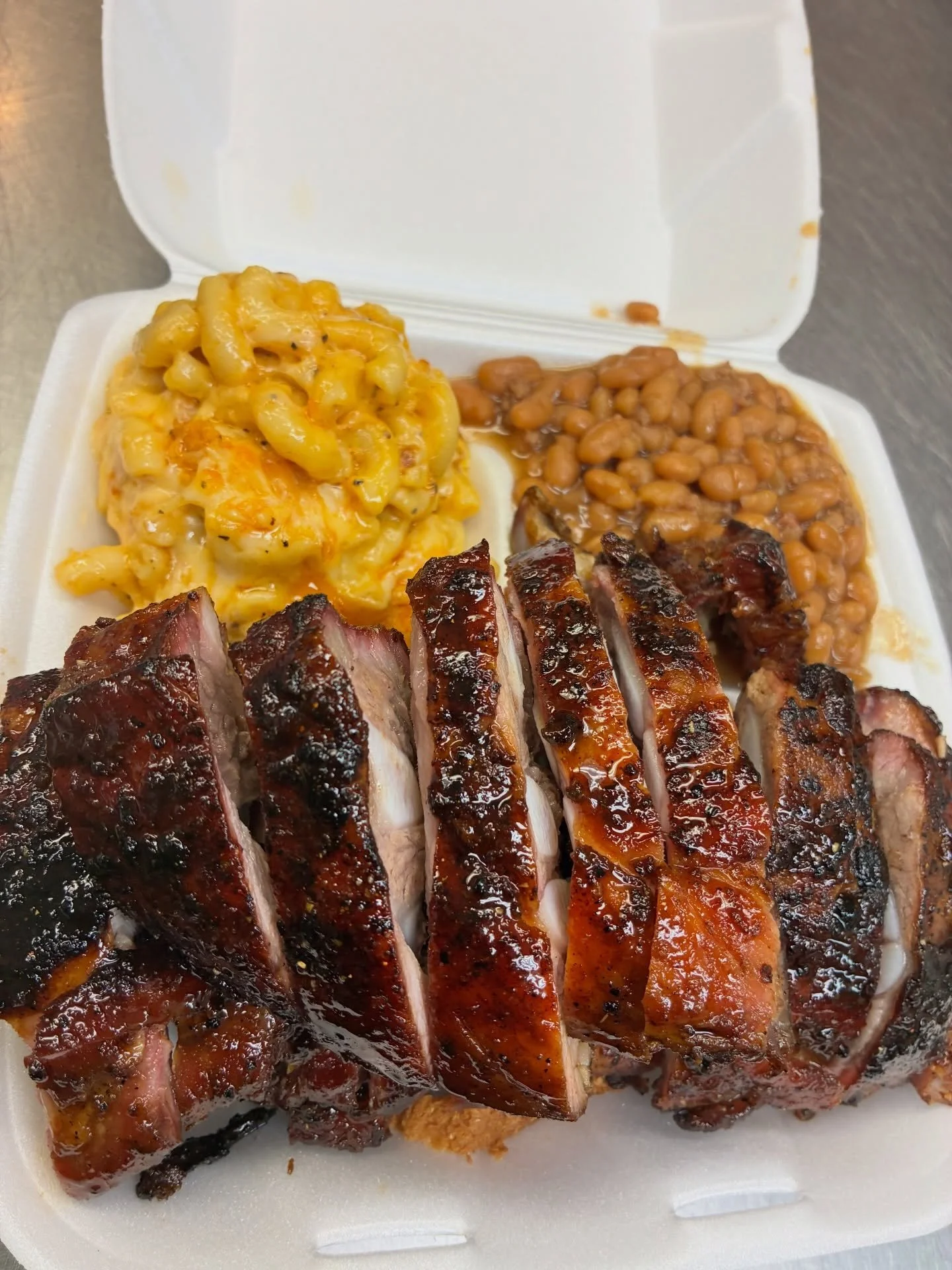 Barbecue ribs with macaroni and cheese, baked beans in foam takeout container.