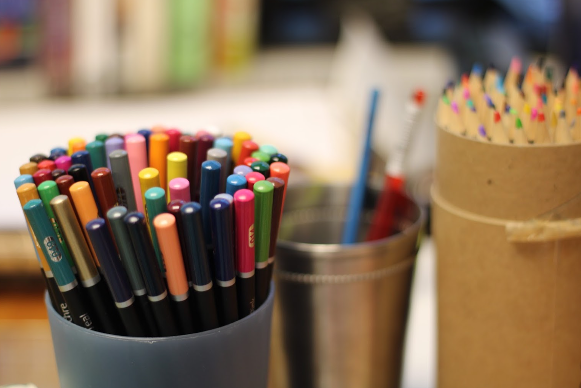 Collection of colorful markers and colored pencils in containers on a desk.
