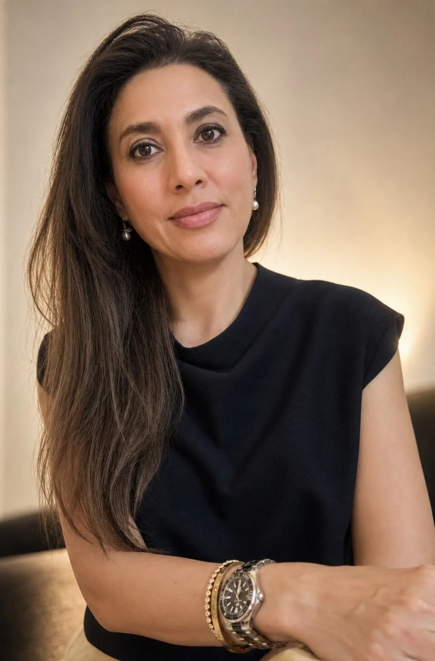Headshot photo of a woman with long dark hair wearing a black top, sitting indoors with a neutral background.