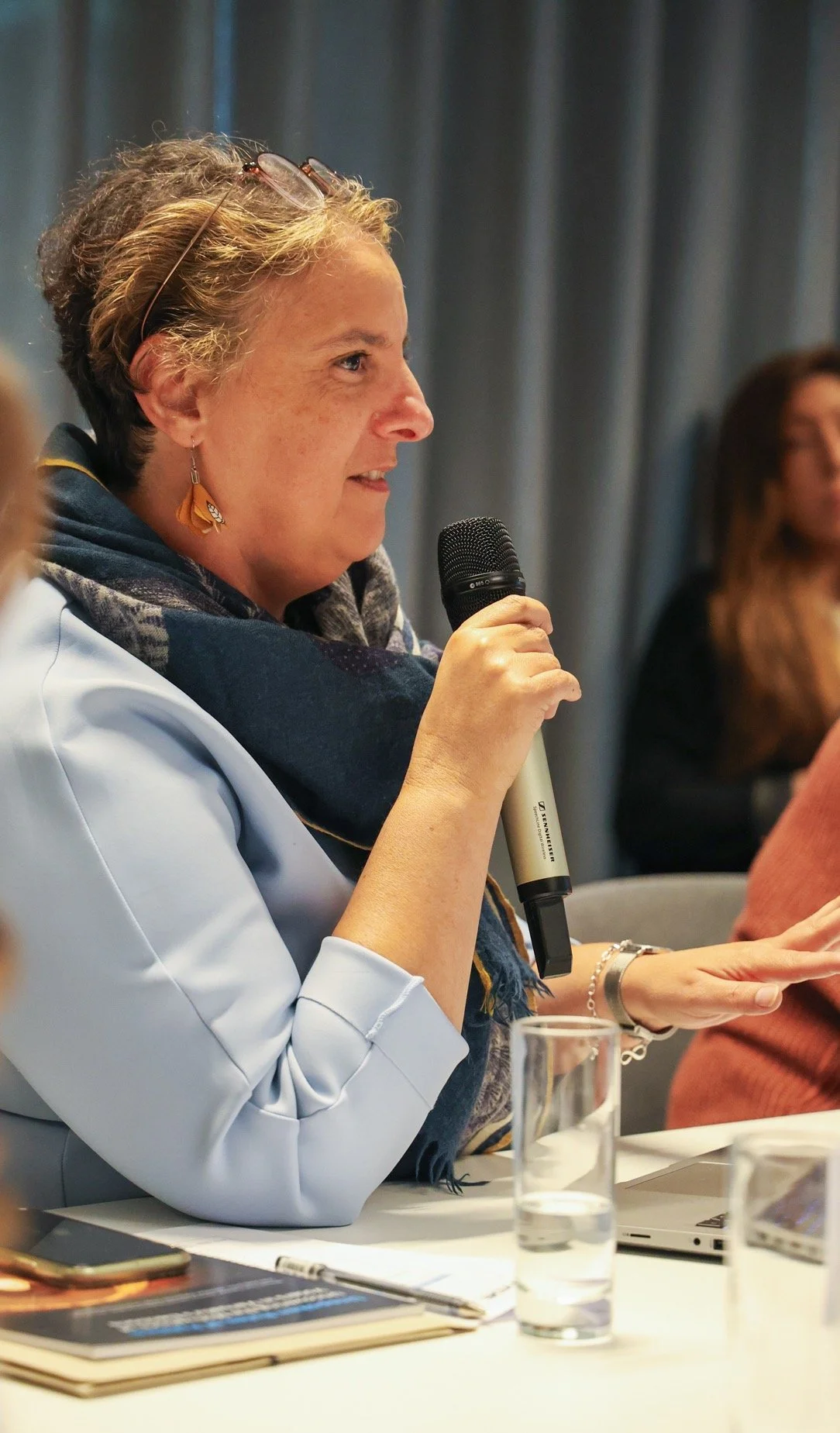 Headshot photo of a woman speaking into a microphone during a meeting or conference.