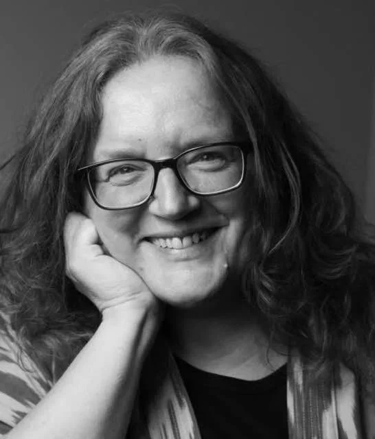 Black and white headshot photo of a woman with glasses, resting her chin on her hand.
