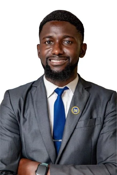 Headshot photo of a man with dark hair and a beard, wearing a gray suit, white shirt, and blue tie, and crossing his arms.