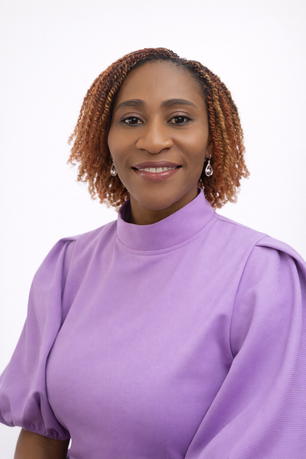 Headshot photo of a woman with curly, reddish-brown hair wearing a lavender top and teardrop earrings, against a plain white background.