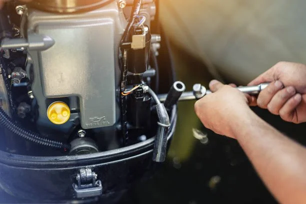 A person using a wrench to work on an outboard motor engine on a boat.