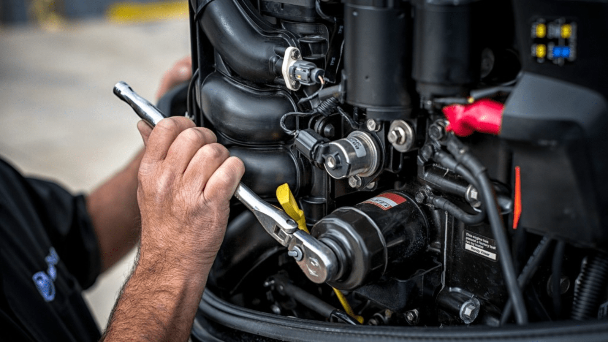 Person working on a boat engine, using a wrench to tighten a bolt.