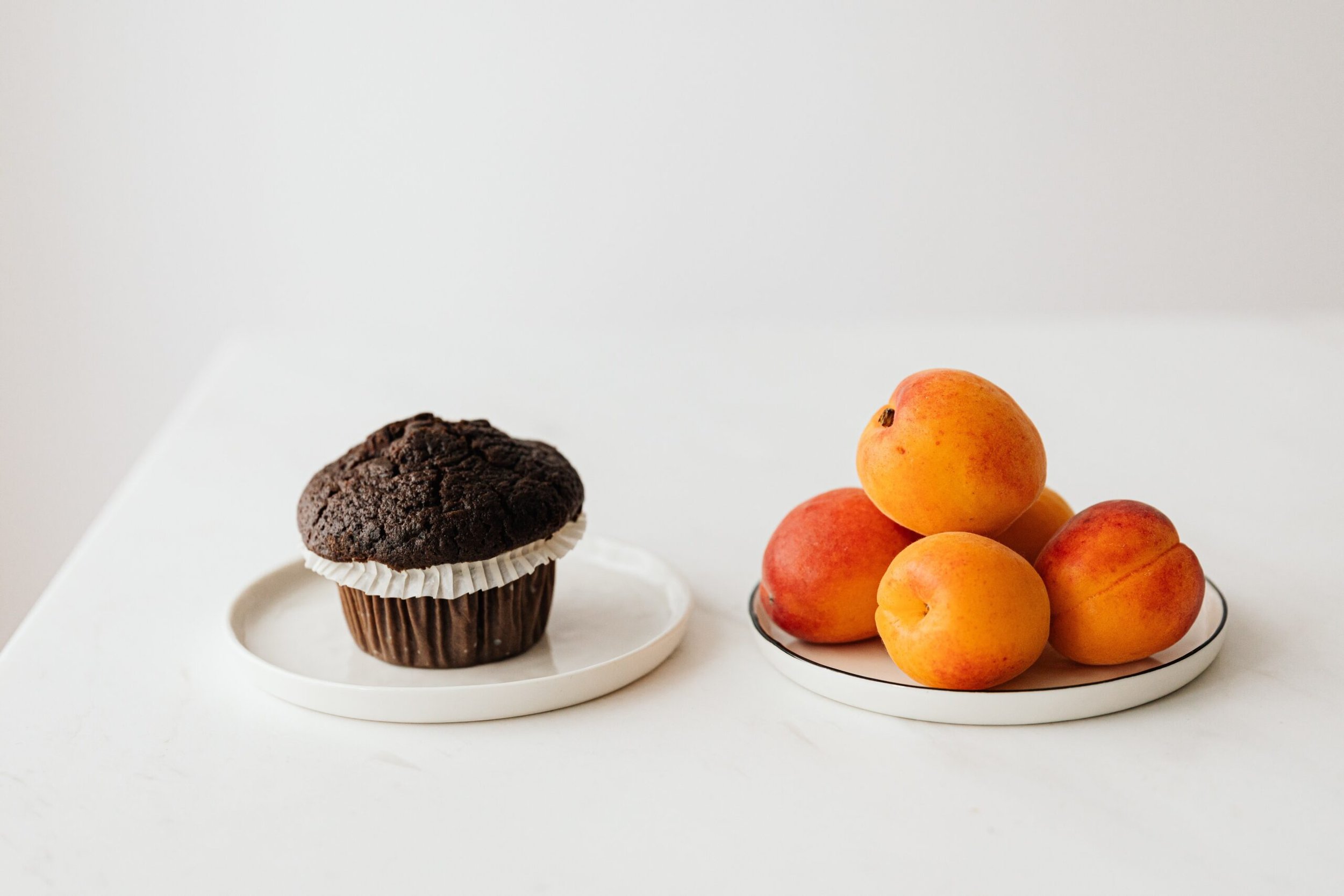 A chocolate muffin and a fresh orange on white plates, illustrating food neutrality and balanced nutrition in eating disorder recovery with Shannon O'Keefe, RCC.