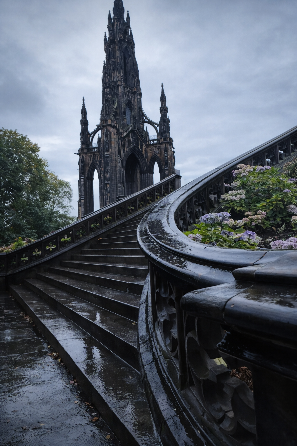 A steep, wet staircase with ornate black railings, leading up to a gothic-style tower with intricate details, during a cloudy day with overcast sky and some flowers on the side.