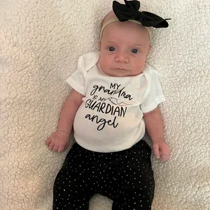 Baby laying on a soft blanket wearing a white onesie with text and black polka dot pants, headband with a bow.