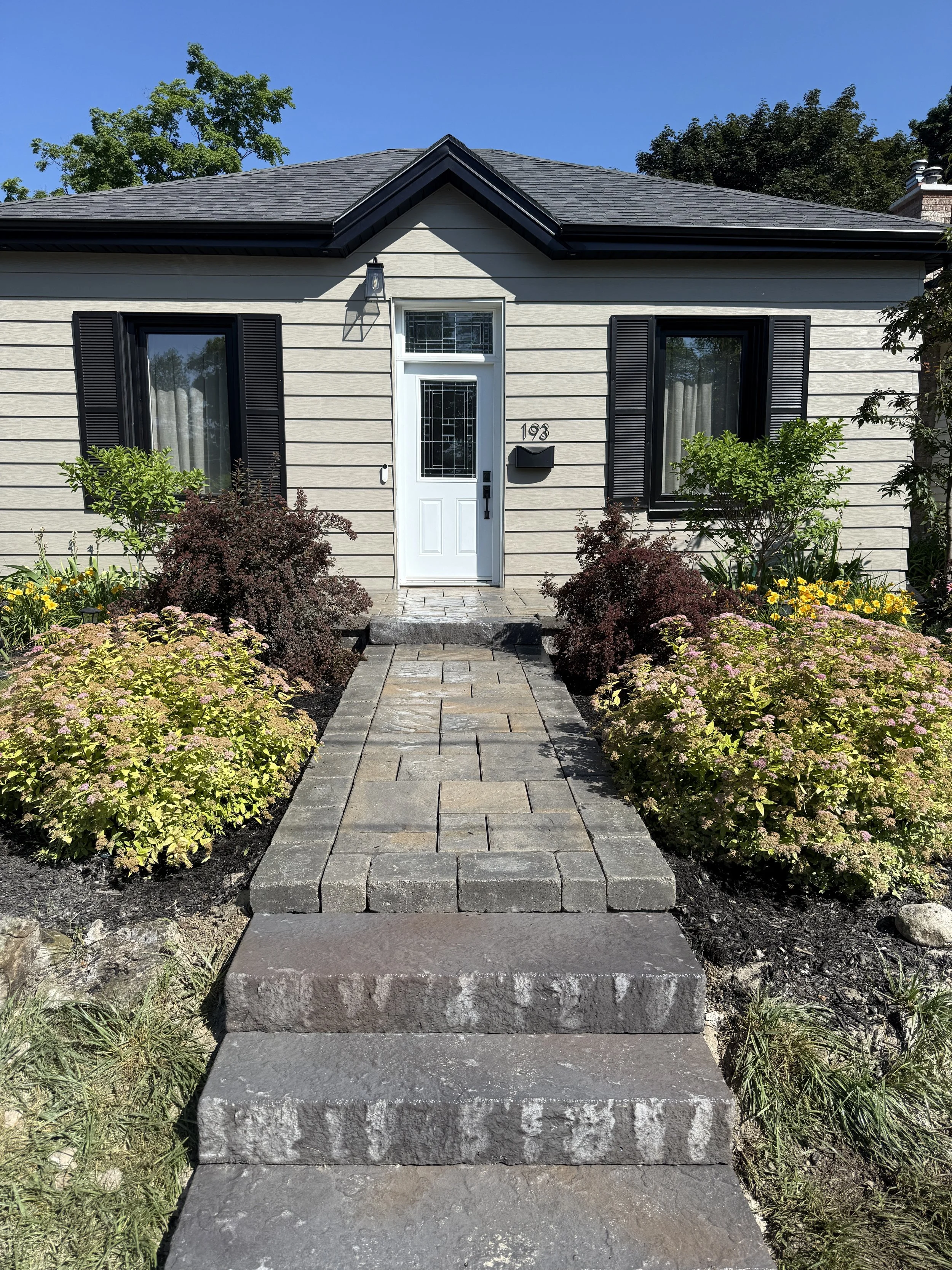 Front view of a house with a stone walkway and landscaped garden with bushes and flowers.