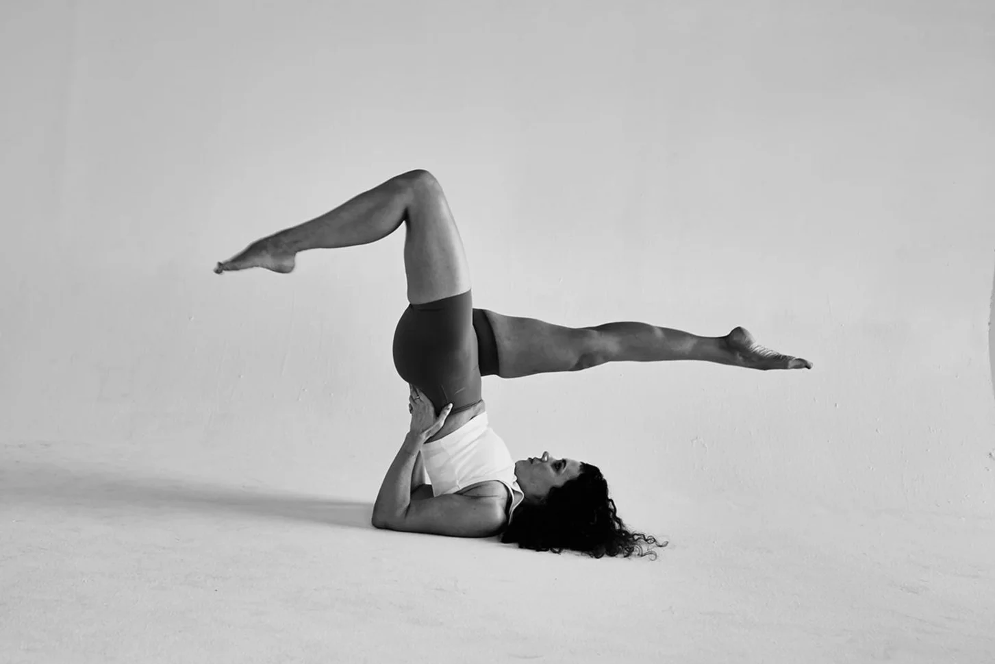 A woman practicing yoga. She is lying on her back with legs extended, supporting a mid-air split with her arms.
