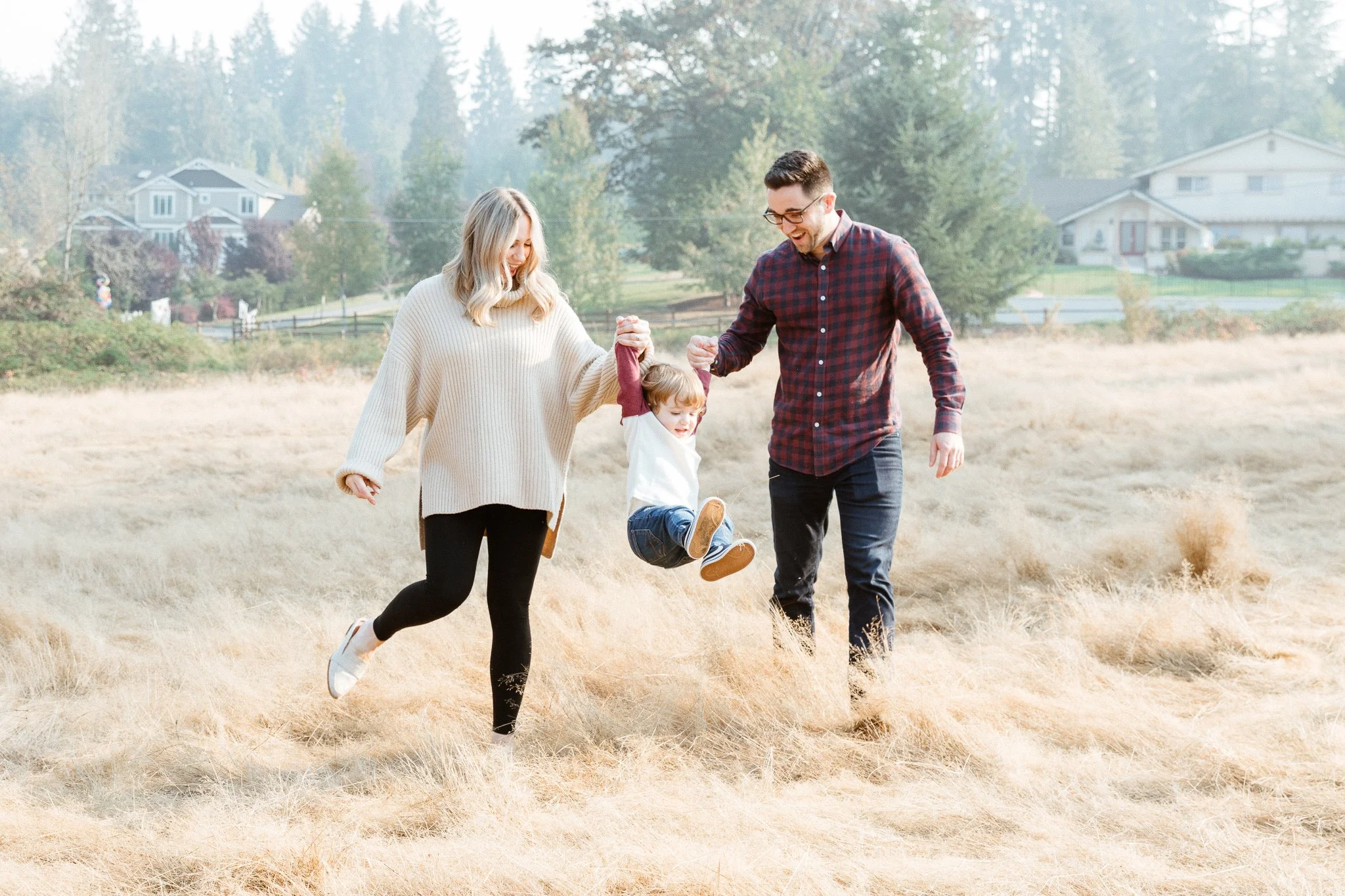 A family of three enjoying outdoor time in a field, with the mother and father holding a young child between them, the girl is being swung in the air.