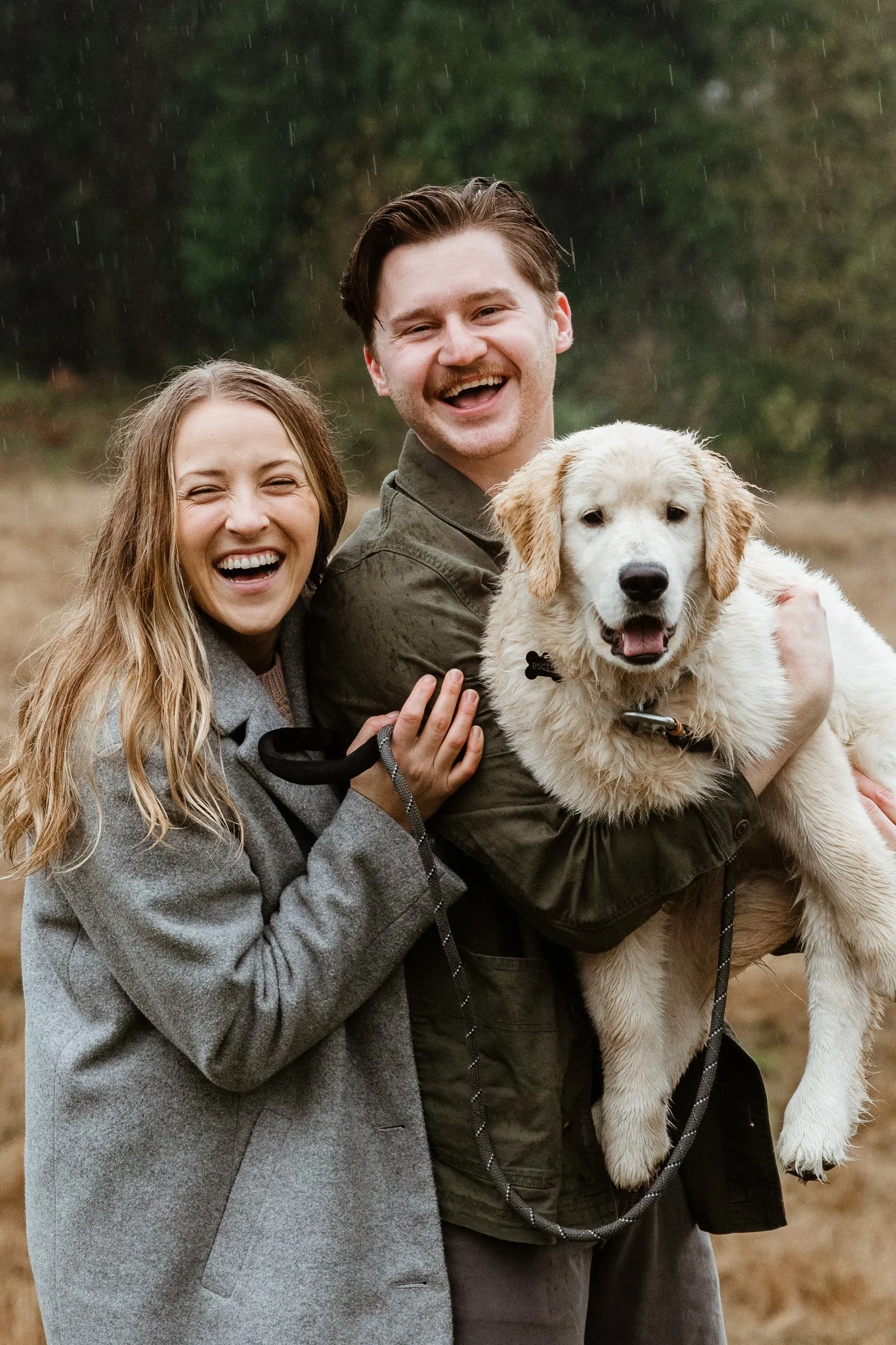 Happy couple with a golden retriever puppy outdoors during rain